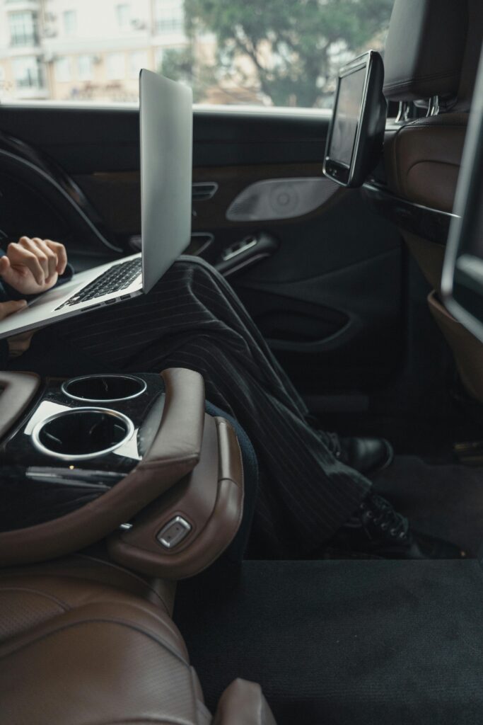 A professional woman working remotely on a laptop inside a luxurious car. Modern executive lifestyle.